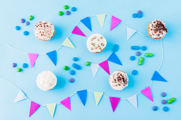 Foto gratuita concepto de cumpleaños con cupcakes; caramelos y empavesado sobre fondo azul