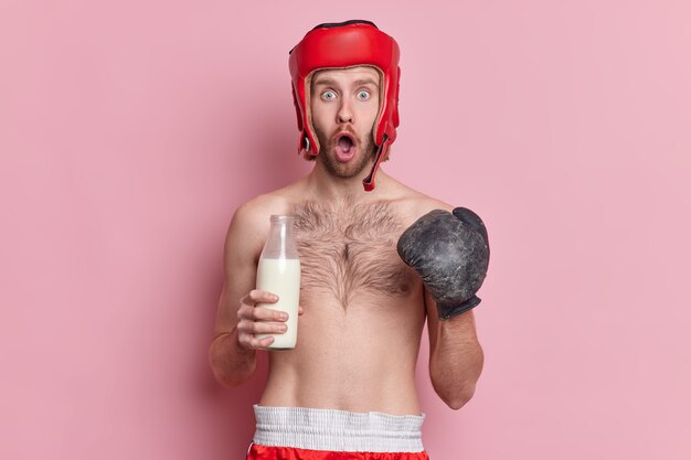 Concepto de deporte y estilo de vida saludable. El hombre sorprendido en el guante de boxeo y el sombrero tiene entrenamiento en el gimnasio mira fijamente impresionado mantiene a la leche de las bebidas de la dieta de la proteína como fuente de calcio.