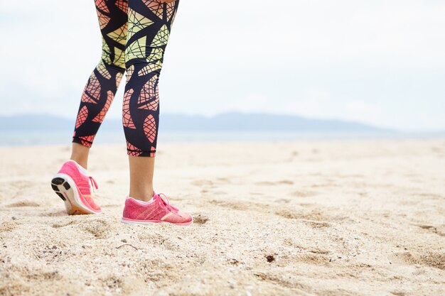 Concepto de deporte y estilo de vida saludable. Toma recortada de las piernas de la atleta chica contra la playa del océano.