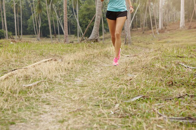 Concepto de deporte y estilo de vida saludable. Vista recortada del corredor mujer bronceada en ropa deportiva y zapatillas de deporte rosa entrenando en zona rural.
