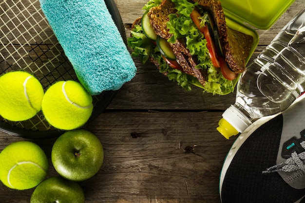 Foto gratuita concepto del deporte de la vida saludable. zapatillas de deporte con pelotas de tenis, toallas, manzanas, sano sandwich y una botella de agua sobre fondo de madera. espacio de la copia. encima.