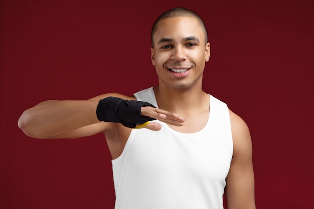 Concepto de deportes, fuerza, poder y motivación. Retrato de guapo joven afroamericano kick-boxer preparando sus puños para la pelea, aplicando vendas de boxeo negras, habiendo concentrado mirada