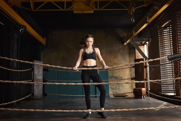 Concepto de determinación, resistencia y fuerza. Disparo de longitud completa de elegante joven mujer caucásica kickboxer vistiendo zapatillas negras, top y leggings