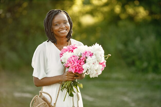 Concepto del día internacional de la mujer. Feliz joven afroamericana con ramo de flores de peonía.