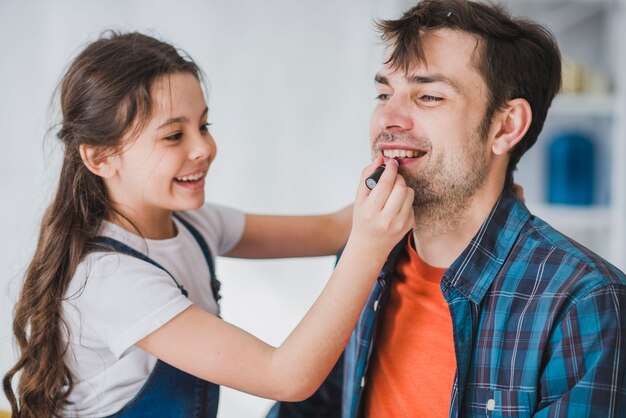 Concepto para el día del padre con hija pintando labios del padre