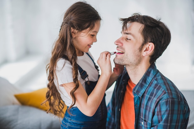 Concepto para el día del padre con hija pintando labios del padre