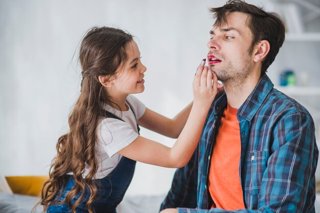 Concepto para el día del padre con hija pintando labios del padre