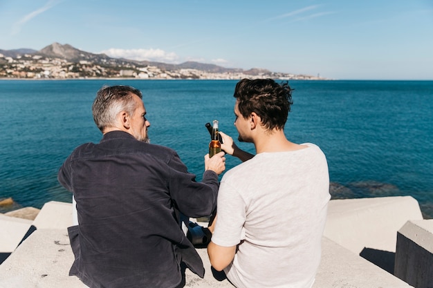 Concepto del día del padre con padre e hijo brindando con cerveza enfrente del océano