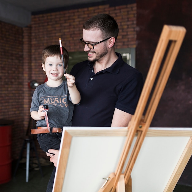 Foto gratuita concepto para el día del padre con padre sonriente e hijo enfrente de lienzo