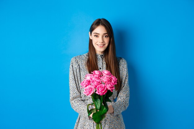 Concepto de día de san valentín tierna mujer joven en vestido sosteniendo ramo de rosas en cita romántica standin ...