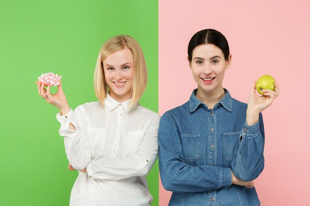 Concepto de dieta. Alimentos saludables y útiles. Hermosas mujeres jóvenes eligiendo entre frutas y pastel poco saludable en el estudio.