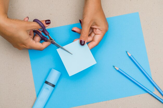 Concepto de educación con útiles escolares en papel, plano lay. Mujer cortando nota adhesiva.