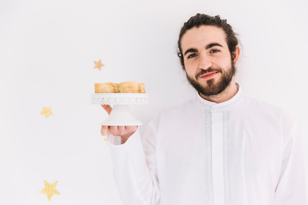 Foto gratuita concepto de eid al-fitr con hombre presentando pasteles árabes