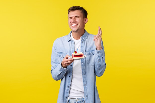 Concepto de emociones de celebración, vacaciones y personas. Chico de feliz cumpleaños soñador celebrando el b-day, sosteniendo el pastel y cerrando los ojos, suplicando que el sueño se haga realidad mientras pide un deseo, cruza los dedos para la buena suerte.