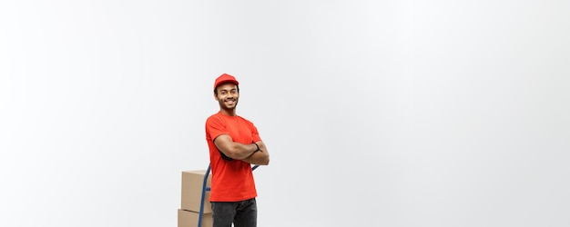 Concepto de entrega Retrato de un apuesto repartidor afroamericano o un mensajero empujando un camión de mano con una pila de cajas aisladas en el espacio de copia de fondo del estudio gris