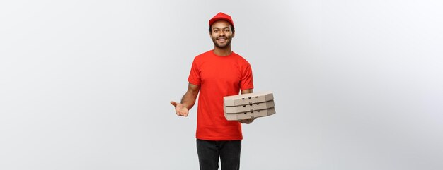 Concepto de entrega Retrato de un apuesto repartidor de pizza afroamericano aislado en el espacio de copia de fondo del estudio gris