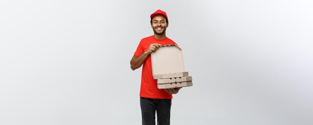 Concepto de entrega Retrato de un apuesto repartidor de pizza afroamericano aislado en el espacio de copia de fondo del estudio gris