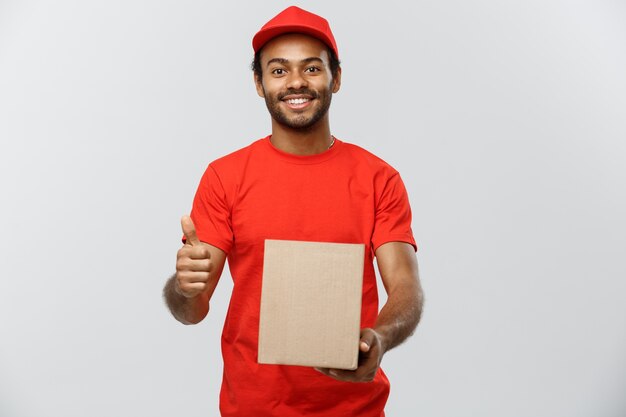 Concepto de entrega - Retrato de feliz africano hombre de entrega de América la celebración de un paquete de caja y mostrando golpes hacia arriba. Aislado en el estudio de fondo gris. Espacio De La Copia.