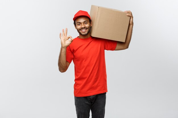 Concepto de entrega - Retrato de feliz africano hombre de entrega de América celebración de paquetes de la caja y mostrando golpes hacia arriba. Aislado en el estudio de fondo gris. Espacio De La Copia.