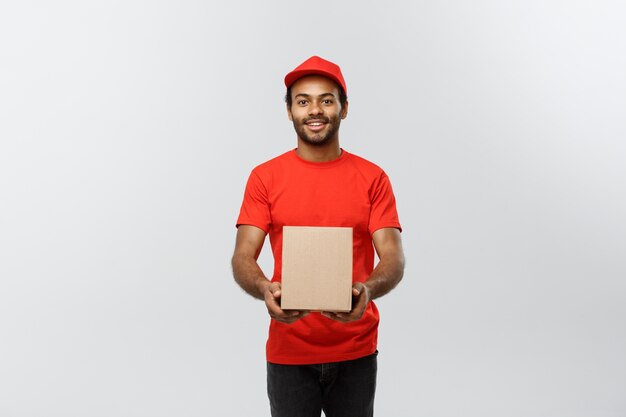 Concepto de entrega - Retrato de feliz africano hombre de entrega de América en tela roja celebración de un paquete de caja. Aislado en el estudio de fondo gris. Espacio De La Copia.