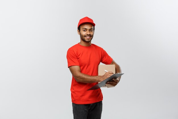 Concepto de entrega - Retrato de feliz africano hombre de entrega de América en tela roja celebración de un paquete de caja. Aislado en el estudio de fondo gris. Espacio De La Copia.