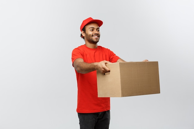 Concepto de entrega - Retrato de feliz africano hombre de entrega de América en tela roja celebración de un paquete de caja. Aislado en el estudio de fondo gris. Espacio De La Copia.