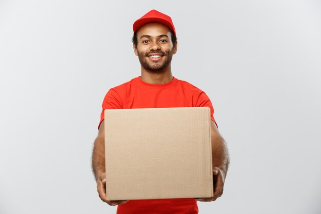 Concepto de entrega - Retrato de feliz africano hombre de entrega de América en tela roja celebración de un paquete de caja. Aislado en el estudio de fondo gris. Espacio De La Copia.