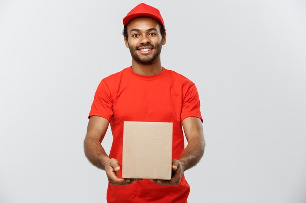 Concepto de entrega - Retrato de feliz africano hombre de entrega de América en tela roja celebración de un paquete de caja. Aislado en el estudio de fondo gris. Espacio De La Copia.