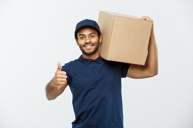 Concepto de entrega - Retrato de feliz africano hombre de entrega de América en tela roja celebración de un paquete de caja. Aislado en el estudio de fondo gris. Espacio De La Copia.