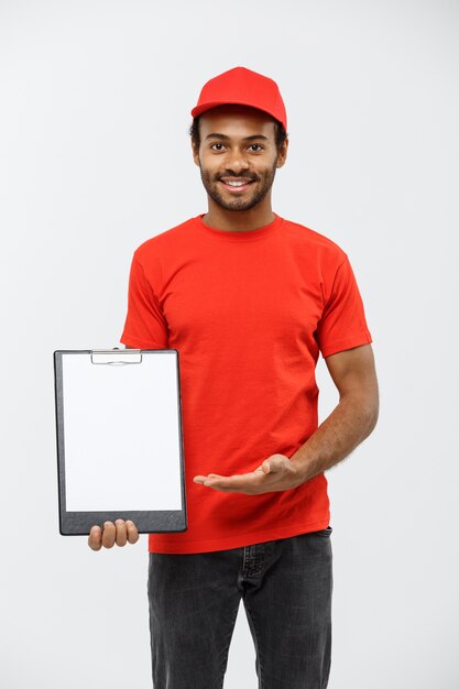 Concepto de entrega - Retrato de hermoso African American entrega hombre o mensajero mostrando un formulario de documento de confirmación de firmar. Aislado en el estudio de fondo gris. Espacio De La Copia.