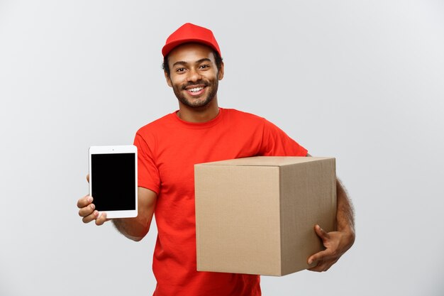 Concepto de entrega - Retrato de hermoso African American hombre de entrega o mensajero con cuadro que muestra la tableta sobre usted para comprobar la orden. Aislado en el estudio de fondo gris. Espacio De La Copia.