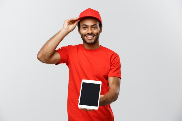 Concepto de entrega - Retrato de hermoso African American hombre de entrega o mensajero con cuadro que muestra la tableta sobre usted para comprobar la orden. Aislado en el estudio de fondo gris. Espacio De La Copia.