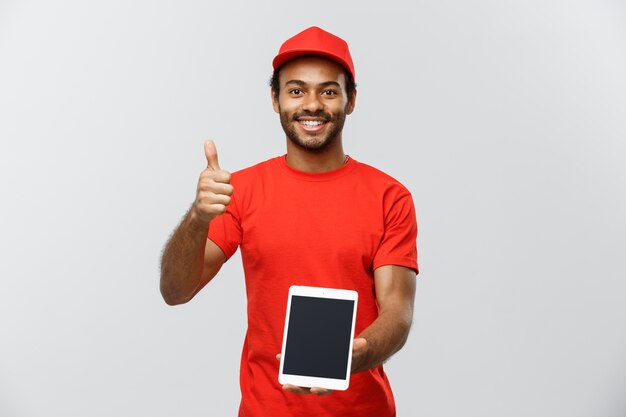 Concepto de entrega - Retrato de hermoso African American hombre de entrega o mensajero con cuadro que muestra la tableta sobre usted para comprobar la orden. Aislado en el estudio de fondo gris. Espacio De La Copia.