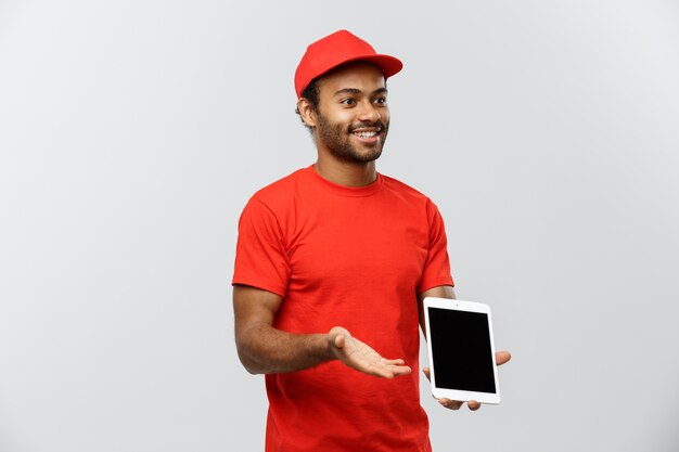 Concepto de entrega - Retrato de hermoso African American hombre de entrega o mensajero con cuadro que muestra la tableta sobre usted para comprobar la orden. Aislado en el estudio de fondo gris. Espacio De La Copia.