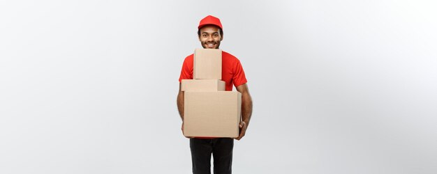 Concepto de entrega Retrato del repartidor afroamericano feliz en tela roja sosteniendo un paquete de caja aislado en el espacio de copia de fondo de estudio gris