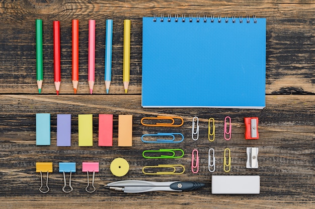 Concepto de escolarización posterior a la pandemia con cuaderno, surtido de útiles escolares en mesa de madera plana.