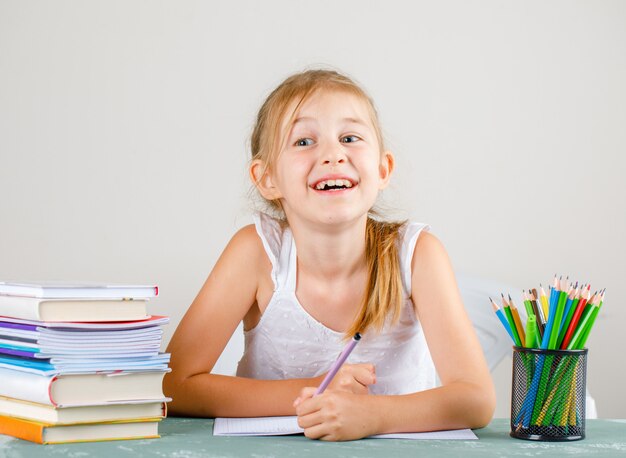 Concepto de escuela con lápices, libros, cuadernos vista lateral. Niña con lápiz.