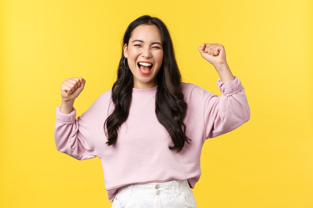 Concepto de estilo de vida, emociones y publicidad. Feliz niña asiática sonriente y bombeada celebrando la victoria, cantando sí con las manos levantadas y una amplia sonrisa, triunfando sobre los logros o el éxito.