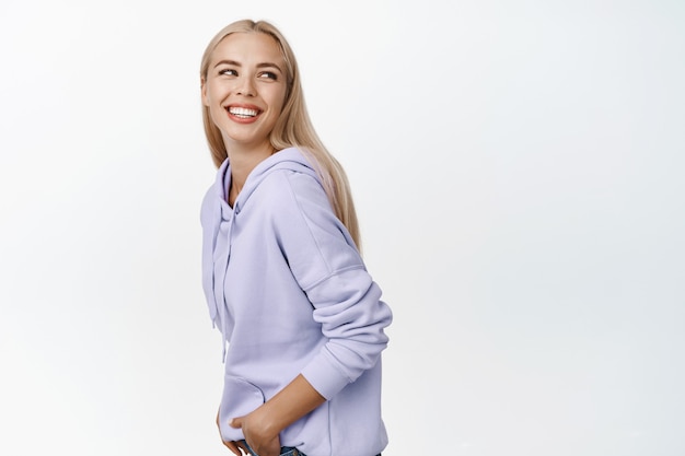 Concepto de estilo de vida y personas. Sonriente mujer natural mirando detrás de su hombro y riendo, feliz de pie en blanco.