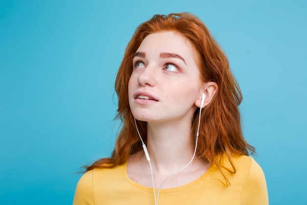 Concepto de estilo de vida - Retrato de alegre alegre pelo rojo jengibre niña disfrutar de escuchar música con auriculares sonriendo alegre a la cámara. Aislado en el fondo azul Pastel. Copie el espacio.