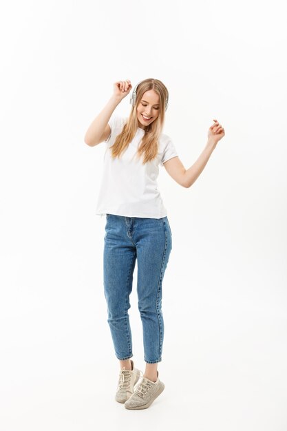 Concepto de estilo de vida: Retrato de una estudiante alegre y feliz escuchando música con auriculares mientras baila aislado sobre fondo blanco.