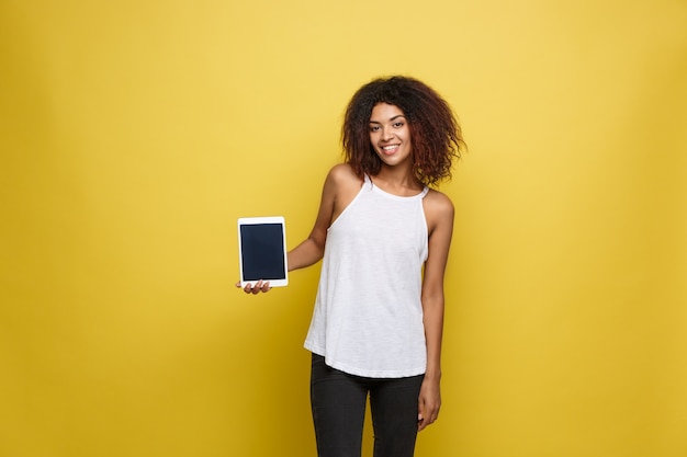 Concepto de estilo de vida - Retrato de hermosa mujer afroamericana alegre jugando algo en tableta electrónica. Fondo amarillo pastel del estudio. Espacio De La Copia.