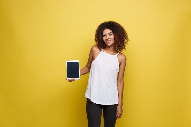 Concepto de estilo de vida - Retrato de hermosa mujer afroamericana alegre jugando algo en tableta electrónica. Fondo amarillo pastel del estudio. Espacio De La Copia.