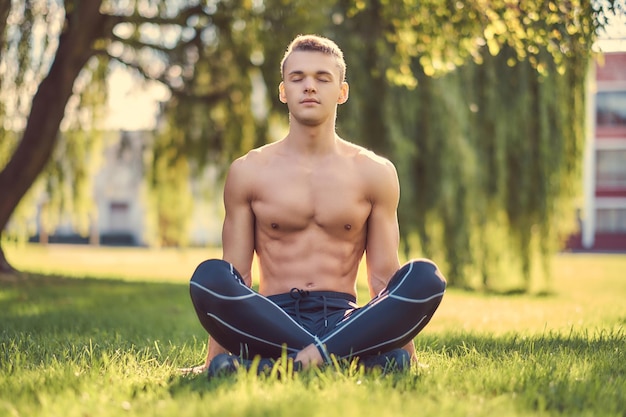 Concepto de estilo de vida saludable. Un joven sin camisa meditando en una pose de loto sentado en una hierba verde.