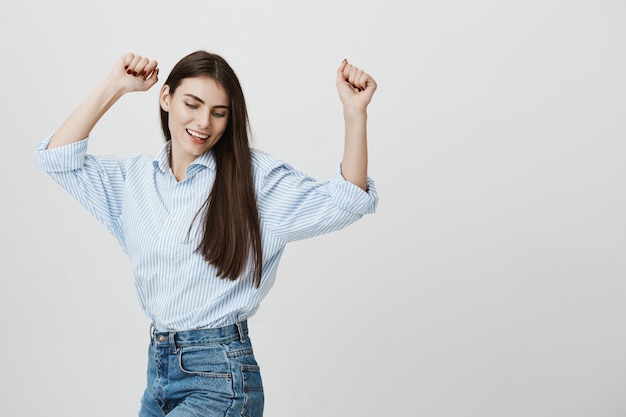 Concepto de éxito y felicidad. Mujer atractiva en camisa bailando con las manos arriba