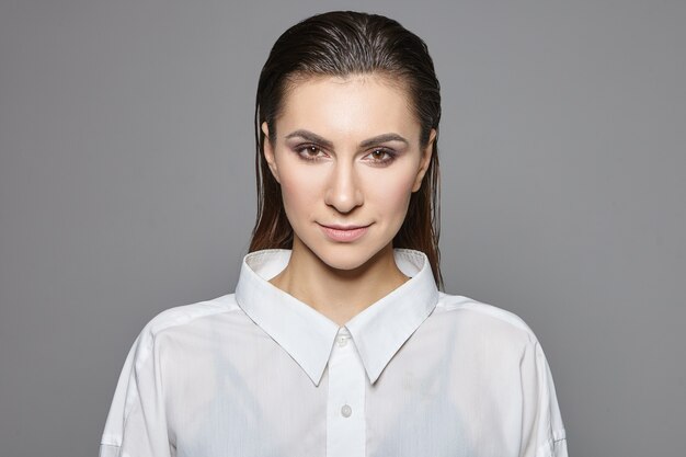 Concepto de feminidad, masculinidad y androginia. Disparo aislado de exitosa hermosa joven empresaria morena en elegante camisa blanca formal mirando con expresión de confianza, sonriendo