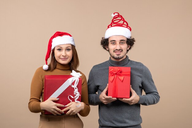 Concepto festivo de humor de año nuevo con divertida feliz pareja encantadora satisfecha con sombreros rojos de santa claus en gris