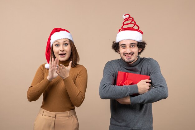 Concepto festivo de humor de año nuevo con divertida pareja encantadora feliz con sombreros rojos de santa claus en gris