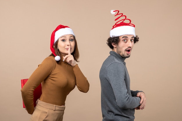 Concepto festivo de humor de año nuevo con divertida pareja encantadora con sombreros rojos de santa claus chica haciendo sorpresa