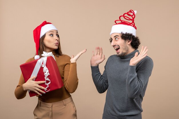 Concepto festivo de humor de año nuevo con divertida pareja encantadora con sombreros rojos de santa claus enviando beso a niña en gris